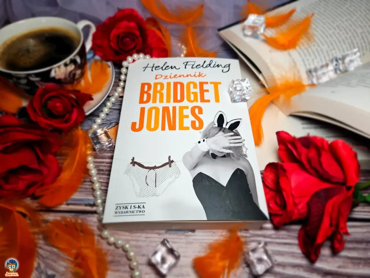 Kto jest autorem popularnej książki Dziennik Bridget Jones? To Helen Fielding. Obok książki kawa, róże i pióra.